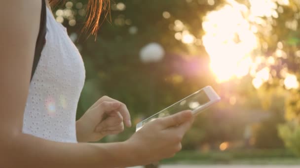 Una giovane ragazza tiene in mano un tablet moderno nell'abbagliamento del tramonto, va online su Internet, i raggi del sole brillano sul touch screen del tablet, il concetto di tecnologie moderne — Video Stock