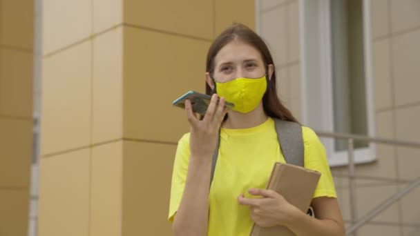 Schoolmeisje meisje in een masker met een rugzak gesprekken op een smartphone online, moderne trends in de technologische vooruitgang, zichzelf te beschermen tegen coronavirus infectie, luchtfiltratie — Stockvideo
