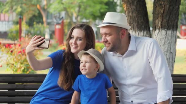 Famiglia felice stanno sorridendo fanno selfie al telefono, padre madre e bambino sono fotografati su uno smartphone, madre, padre e figlio comunicano via videochiamata online, amano il bambino piccolo, la gente di città — Video Stock
