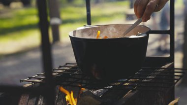 Elinle tencerede yemek karıştırmak, doğada kamp gezisinde yemek pişirmek, ateş ve sigara üzerine yemek tarifleri, hafta sonları modern açık hava aktiviteleri, tencereden çıkan sıcak buhar.