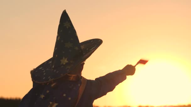Мальчик в шляпе вызывает волшебную палочку на закате, галлюцинации, верит в детскую магию, ребенок играет в сиянии солнца, детские карнавальные костюмы для праздника, астраномный праздничный наряд, детская мечта — стоковое видео