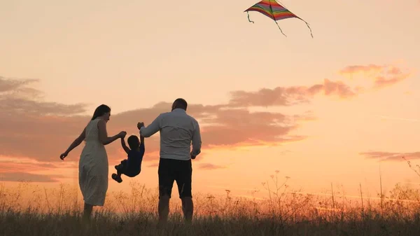 Happy family day, father mother and little kid fly a kite into the sky at sunset, play with child in nature in the evening, love spending time with family, raising and developing baby, cheerful life. — Stock Photo, Image