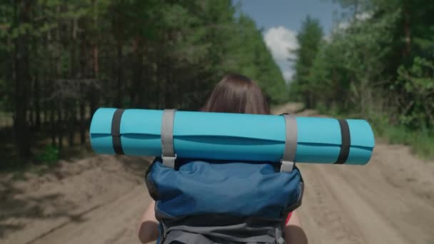 Ung flicka reser genom skogen med en ryggsäck på axlarna, en tusenårig vandring i parken, en aktiv frisk flicka i en motiverad äventyr, en glad dag ledigt — Stockvideo