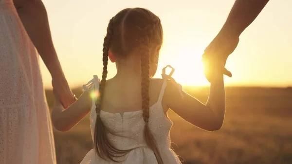 Cheerful girl holding her parents hands at sunset in sky, happy family, childhood dream, child with mom and dad in sun, little kid walks with father mother, family day, travel with baby hand in hand — Stock Photo, Image