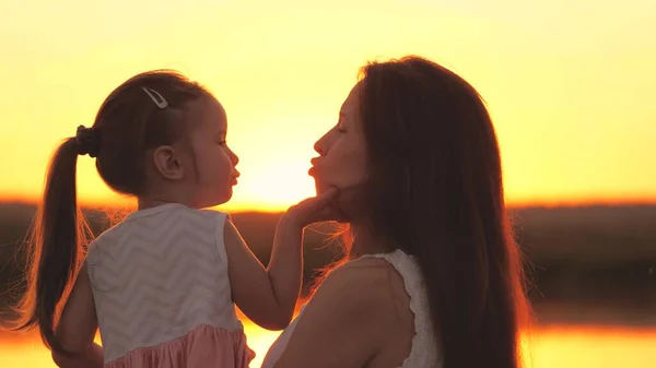 little girl kisses her mother at sunset, happy family, childhood dream, mom hugs her beloved daughter in the rays of sunshine, kids trip on a weekend with a parent, kissing baby on the lips