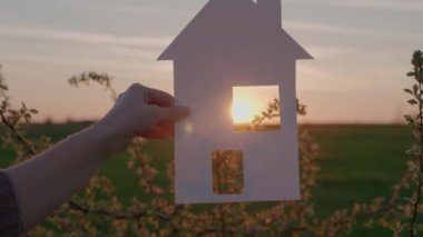 Gün batımında bir kağıt evi elinde tutmak, genç bir aileye ipotek kredisi vermek, pencereden süzülen bir güneş ışığı, yeni bir ev almak, ev sahibi olmak, yaşamak için emlak kiralamak.