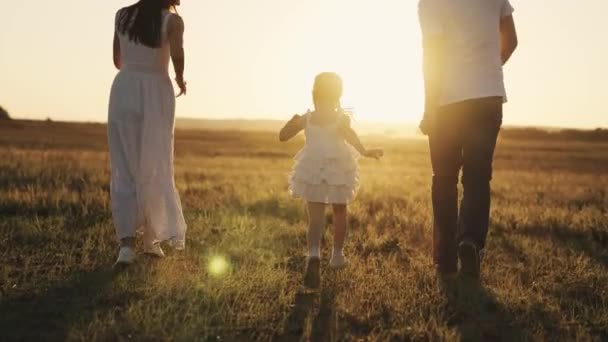 Маленька смішна дівчинка біжить зі своїми батьками на заході сонця, щасливою сім'єю, дитячою мрією, дитиною, бігає на сонці з мамою і татом, грає з дитиною, батьком і матір'ю з дочкою-немовлям — стокове відео