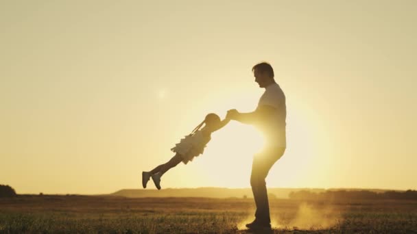 Pappa cirklar runt en liten dotter vid solnedgången på himlen, en glad unge svävar i flykt över jorden i solens strålar, barnet med sin far leker pilot, lycklig familj, silhuett av man och flicka — Stockvideo