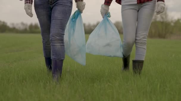緑の芝生の上にゴミ袋を持っている男、不必要な廃棄物の収集と処分、掃除作業のための手袋の女性、惑星環境の保護、地球をきれいにするのに役立ちます — ストック動画