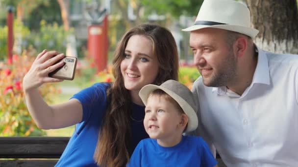 Glückliche Familie lächelt macht Selfie am Telefon, Vater Mutter und Kind werden mit dem Smartphone fotografiert, Mutter, Vater und Sohn kommunizieren per Videoanruf online, lieben das kleine Kind, Stadtmenschen — Stockvideo