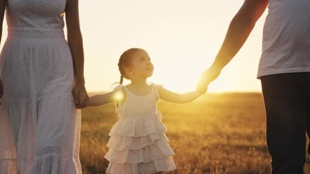 Menina leva sua mãe e pai pela mão ao pôr do sol, uma pequena filha com seus pais ao sol, de mãos dadas, uma família feliz, uma criança com mãe e pai, cuidar e amar o bebê — Vídeo de Stock