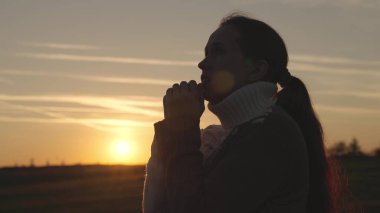 Gün batımında gökyüzünde dua eden bir kız, yardım isteyen bir kadının silueti, güneşin altında namaz kılan, inanan biri olarak yaşayan, şafakta Ramazan ayı, ellerinin avuçlarıyla meditasyon yapan.