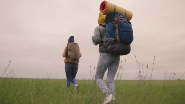 Happy active hipster girls with backpacks on their backs travel through a beautiful valley, a millennial woman on a green field, travel hiking, hiking on the trail, outdoor recreation — Stock Video