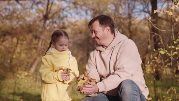 Otec s malým dítětem v městském parku házet žluté listí nahoru, šťastná rodina, dívka s otcem hrát venku v podzimním lese, dobrá emocionální nálada, veselý smích na Den otců — Stock video