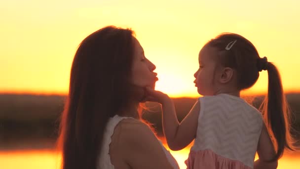 Klein meisje kust haar moeder bij zonsondergang, gelukkig gezin, kinderdroom, moeder knuffelt haar geliefde dochter in de stralen van de zon, kinderen struikelen in een weekend met een ouder, zoenen baby op de lippen — Stockvideo