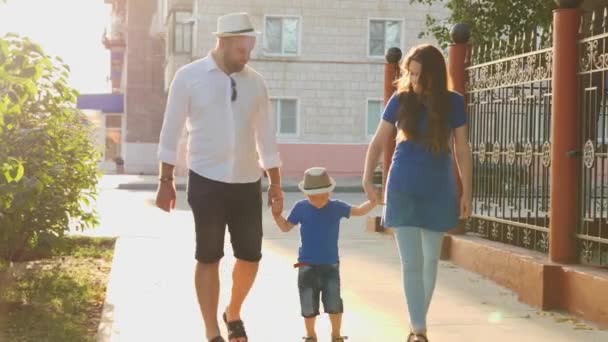 Gelukkig ouders met kleine zoon lopen rond in de stad bij zonsondergang, een jongen springt hoog van de grond, vrolijk kind met zijn vader en moeder spelen samen superheld, kind met mam en pap reizen in het licht van de zon — Stockvideo