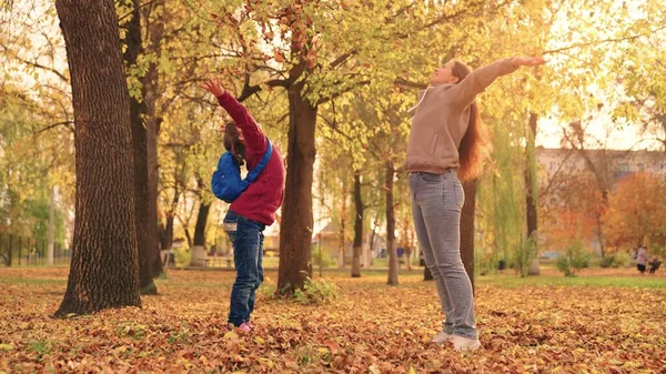 Mother and little child in an autumn park throw dry leaves up, happy family, live fun with mom, cheerful kid plays with foliage and parent hands throwing leaf fall, parental care of girl, nature walk — Stock Photo, Image