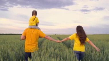 Karısı ve küçük çocuğuyla birlikte bir çiftçi yeşil bir buğday tarlasında yürüyor, mutlu bir aile, bir babaya binme hayali, aile işi, çavdar tarlası, tahıl üretimi