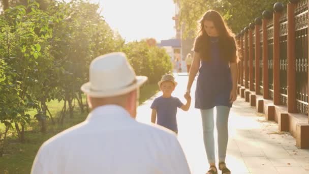 Boy runs to hug dad at sunset, happy family, little son in arms of his beloved father in glare of sun, mother and child in city park for walk, love life, meet and have fun, family weekend vacation — Stock Video