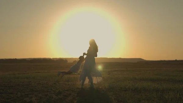 Moeder cirkelt rond haar dochtertje bij zonsondergang in het veld, een vrolijk kind vliegt in de lucht in de zon, spelen superheld, gelukkig gezin, moeders liefde voor een kind, een wandeling met baby in de natuur — Stockfoto