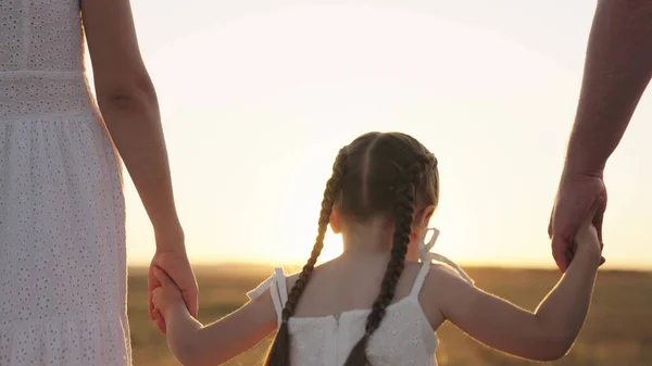 Liten unge håller sin far och mor för hand vid solnedgången, lycklig familj, ha kul och leka med föräldrar i parken, bra barn liv med snäll mamma och pappa, fantasi barndomsdröm, baby utomhus i naturen — Stockfoto