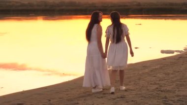 Mutlu kadın arkadaşlar gün batımında sahilde yürürler, genç anne ve yetişkin bir kız güneş ışınları altında, mutlu aile, neşeli insan, hayat arkadaşı, nazik atmosferde tavsiyelere yardımcı olur.