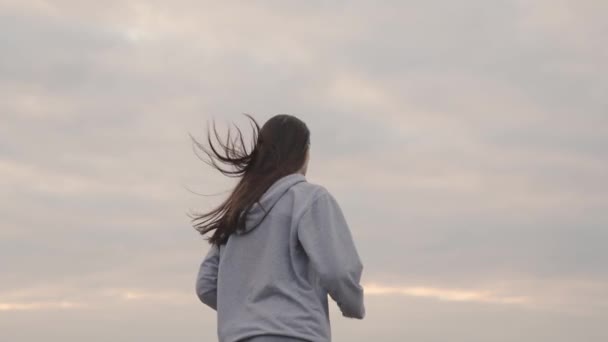 Mädchen in Sportkleidung läuft bei Sonnenuntergang gegen den Himmel, Frauen-Langstreckenjogging, gesunder Lebensstil, Cardio-Training für eine schlanke Figur und ein gesundes Herz, sich bemühen, Erster zu sein, morgens im Morgengrauen laufen — Stockvideo