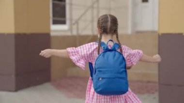 Kız, sırtında bir sırt çantasıyla okula doğru koşuyor, okul çantası birinci sınıf öğrencisinin üstünde, mutlu bir çocuk hemen derse koşuyor, anaokulu eğitimi çocuğu, eğitim kurumlarında eğitim görüyor.