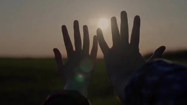 Hands at sunset, lovers reach for the sky, dream of a good, good desire of people, ask for help from the sun, pray in the rays of sunlight, bright glare through the fingers of peoples palms — Stock Photo, Image