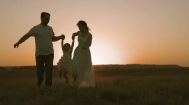 Anne ve babasıyla küçük bir çocuk gün batımında sahada koşuyor, mutlu aile, ebeveynlerle eğlenceli hayat, anne ve baba çocuk yürüyüş için koşuyor, aktif yaşam tarzı, bebek bakımı, aşk ve bakım, takım çalışması.