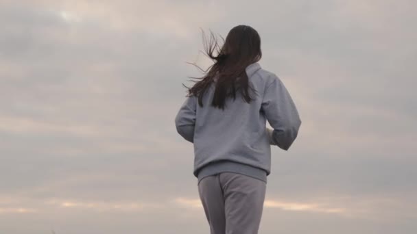 スポーツウェアの女の子は日没時に空に向かって走り、女性は長距離ジョギング、健康的なライフスタイル、スリムな姿と健康な心のための心臓トレーニング、最初になるように努力し、夜明けに朝に実行されます — ストック動画