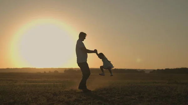 Miły ojciec obraca dziecko o zachodzie słońca, sylwetka szczęśliwej rodziny, wesoły dzieciak bawiący się z tatą w promieniach słońca, dzień ojców, podróż dzieci, spacer z rodzicem, dobre życie — Zdjęcie stockowe