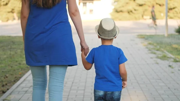 Mutter führt Jungen an der Hand, Sorgerecht für kleines Kind, Mutterglück mit ihrem Sohn, Mutter geht mit Kind im Stadtpark unter freiem Himmel spazieren, Leben mit Eltern, kümmert sich und nimmt sich am Wochenende Zeit für Baby — Stockfoto