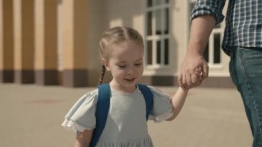 Baba küçük bir kızı okula götürüyor, sırt çantalı bir kız babasının elini tutuyor, bir çocuk okulu eğitim sistemi, mutlu bir aile, mutlu bir ebeveyni olan neşeli bir çocuk