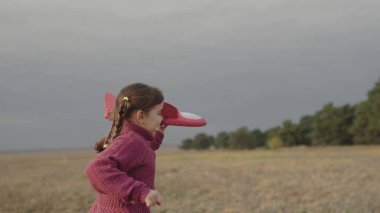 Küçük bir çocuk elinde uçakla sahada koşuyor, çocukluk hayali uçuyor, mutlu bir aile, çocuk gülümsemesi ellerini kanatlarının arasına almış hayal ediyor, neşeli kız pilot olmak istiyor.