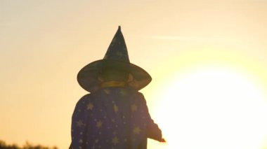 Şapkalı çocuk günbatımında sihirli değnek, halluin, çocuk sihrine inanır, çocuk güneşin parlaklığında oynar, tatil için çocuk karnaval kostümü, astranom şenlik kıyafeti, çocukluk hayali