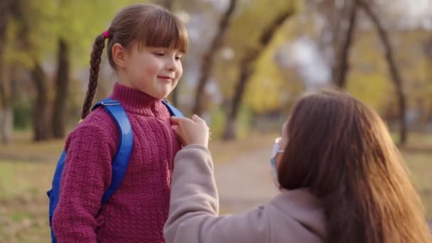 Madre pone un niño pequeño una máscara médica en su cara, protección contra el coronavirus covid 19, niño con mochila, familia feliz, vida pandémica moderna, seguridad para la salud de los estudiantes, gérmenes anti corona, abrazo mamá — Vídeos de Stock