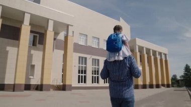 Küçük bir çocuk babasının sırtında okula sırt çantasıyla gidiyor, okul çantalı bir kız ve babası birinci sınıfa gidiyor, mutlu bir aile, okulda ilköğretim görüyor, ailesinden bir çocuk.