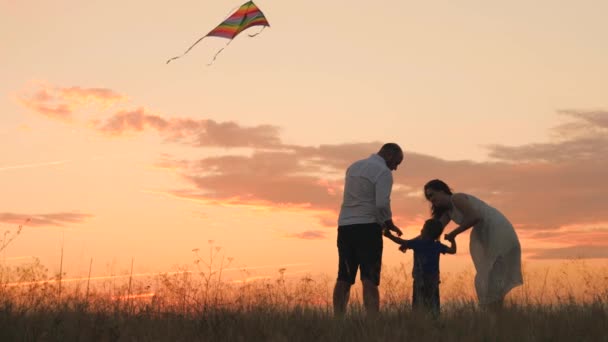 Bonne journée en famille, père mère et petit enfant volent un cerf-volant dans le ciel au coucher du soleil, jouent avec l'enfant dans la nature le soir, aiment passer du temps en famille, élever et développer bébé, vie joyeuse. — Video