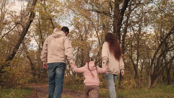 Maman papa et enfant marchent le long de la route d'automne de la forêt, vie familiale heureuse, feuilles sèches jaunes, feuilles tombées dans le parc naturel extérieur, père mère et enfant marchent, fille avec les parents ensemble. — Photo