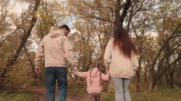 Mama Papa und Kind spazieren auf der Waldherbststraße, glückliches Familienleben, gelbes trockenes Laub, umgefallenes Laub im Naturpark, Vater Mutter und Kind spazieren, Mädchen mit Eltern zusammen. — Stockvideo