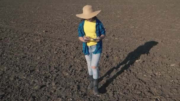 Un agricultor con una tableta camina en un campo arado de tierra con una tableta, el trabajo en una plantación, la agricultura agrícola, un agrónomo se prepara para plantar plántulas en suelo orgánico de la tierra, la producción de negocios — Vídeos de Stock