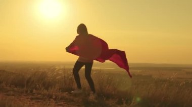 Mutlu genç kız gün batımında süper kahramancılık oynuyor, kırmızı yağmurluk giymiş bir çocuk ışık huzmelerinde, çocuklar rüya görüyor, çocuk güneşin parlaklığında bir süper kahraman olmayı hayal ediyor.