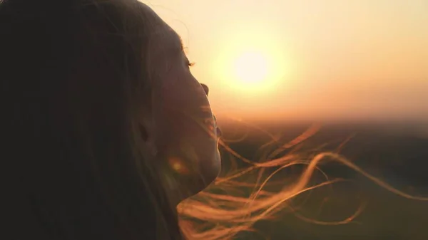 Joven mira el atardecer y reza, persona religiosa, su pelo está volando en el viento en el resplandor del sol, para creer en la bondad, un sueño de las mujeres del amor, para pensar y pedir perdón del cielo — Foto de Stock