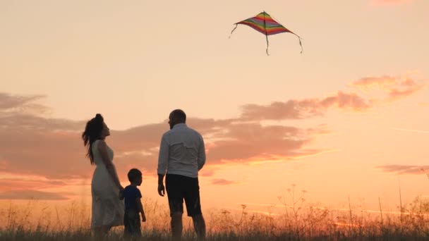 幸せな家族の日、父の母と小さな子供は日没時に空に凧を飛び、夕方には自然の中で子供と遊び、家族と過ごす時間を愛し、赤ちゃんを育て、発達させ、明るい生活. — ストック動画