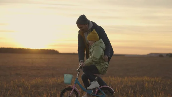 Klein kind leert fietsen met zijn vader bij zonsondergang, gelukkig gezin, kinderdroom om te leren fietsen, kinderpedalen in de zon, meisje en vader lachen plezier tijdens het spelen van het spel, vaderdag — Stockfoto
