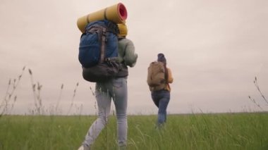 Sırtlarında sırt çantaları olan mutlu, aktif hippi kızlar güzel bir vadide seyahat eder, yeşil bir alanda bin yıllık bir kadın, yürüyüş yapar, patikada yürüyüş yapar, dışarıda dinlenir.