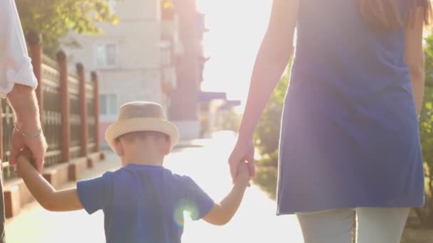Een kleine jongen houdt zijn moeder en vaders handen in de stralen van de zon, wandelen rond de stad met het kind, een gelukkig gezin, moeder, vader en kind in de schittering van de zon, kinderdroom van babys leven — Stockvideo