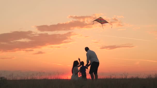 Mom dad and child fly kite at sunset in sky, happy family, father mother and child travel together, childhood dream, family life, little boy walks with his parents in park sunshine, family silhouette — Stock Video