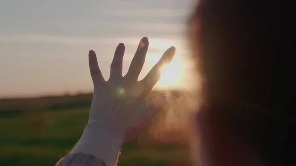 stretching girl hand forward at sunset in sky, praying to sun, traveling on a weekend vacation in rays of light, hiking in nature, relaxing rejoicing in glare of dawn, light through your fingers